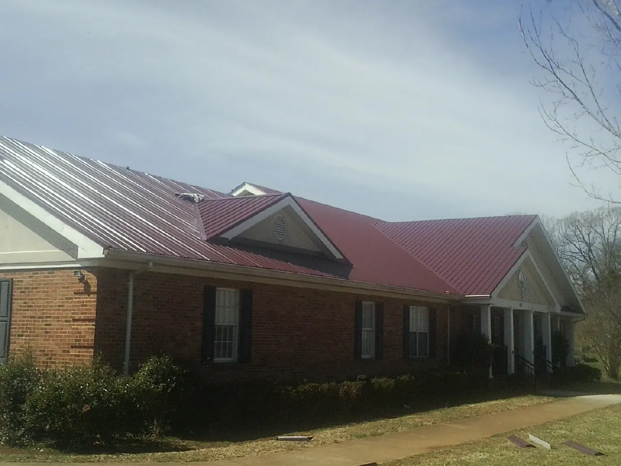 Red metal roof with gabled entries on a long brick building, from a Hail Damage Roof Repair job in Pineview