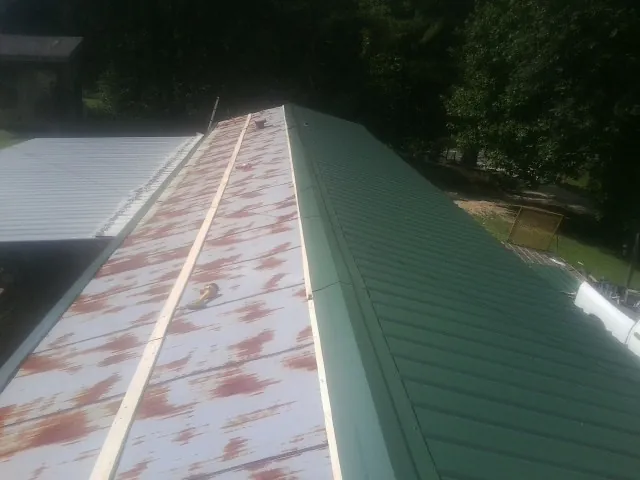 Old rusted panels beside newly installed green metal roofing in Pineview