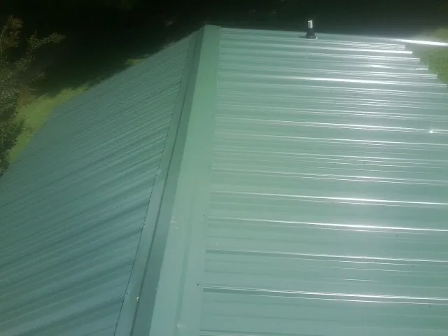 New green metal panels meeting at the ridge of a roof — Flat Roof Repair work by our crew in Pineview
