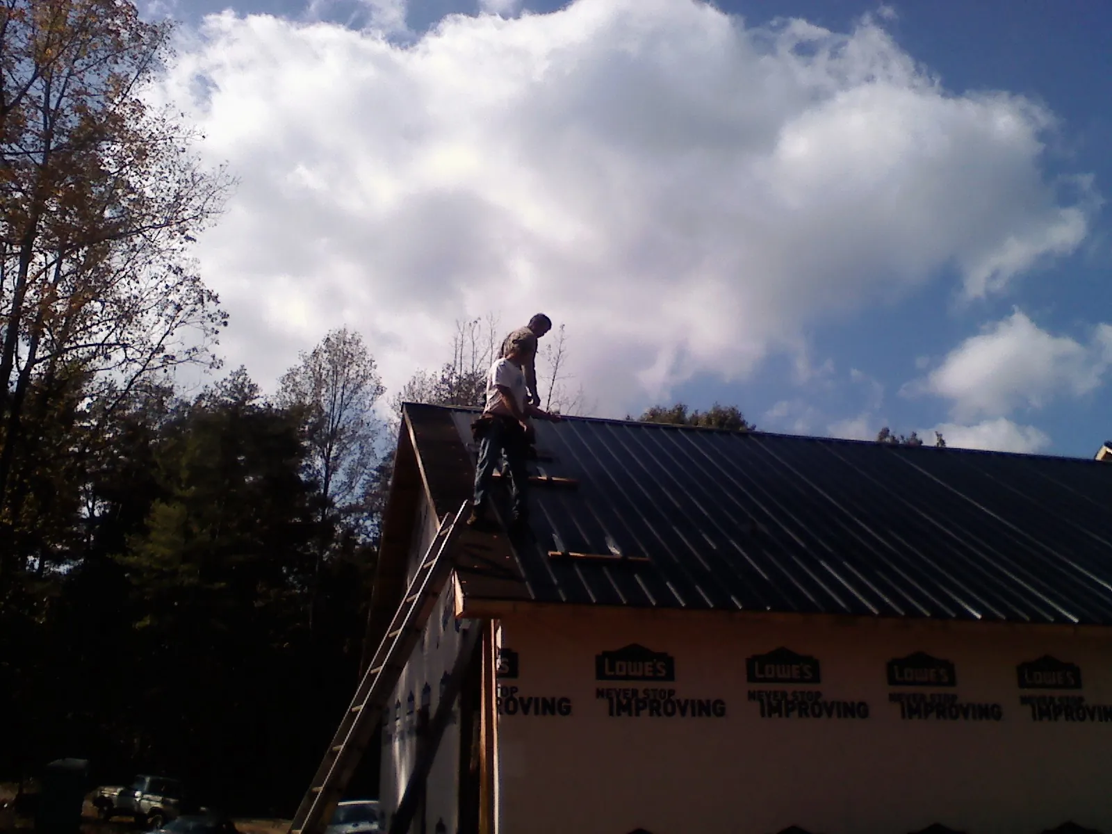 Roofer fastening dark metal panels high against a cloudy sky, from a Roof Inspection job in Pineview
