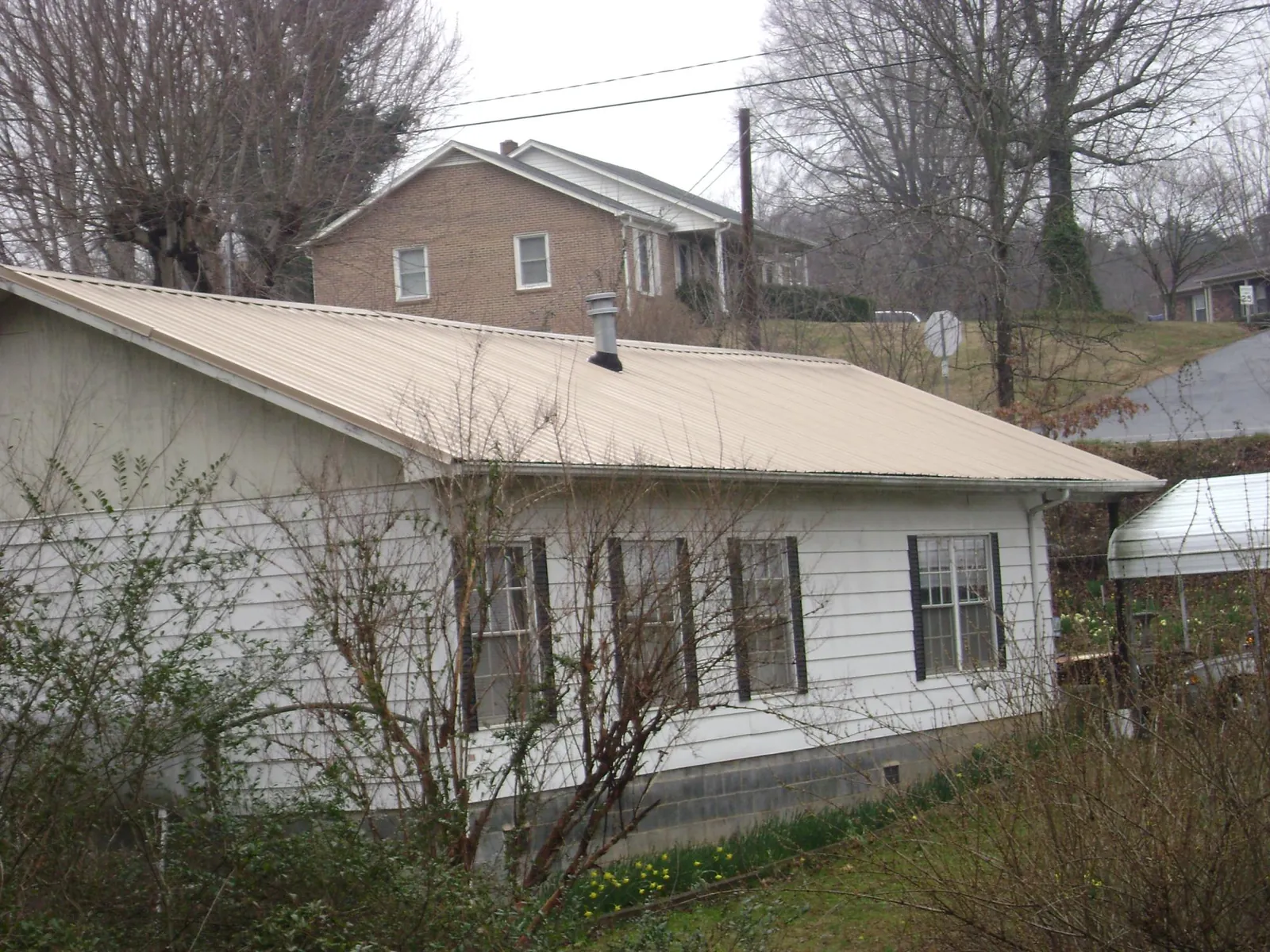Tan metal roof on a white sided house set into a hillside — Commercial Roofing by Roofing Brothers in Pineview